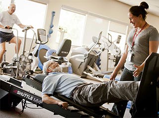 Physical therapist at Presbyterian Healthplex helps patient with rehabilitation and strengthening on exercise machines.