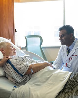 Presbyterian surgical oncologist talks with a cancer patient at bedside about the patient’s cancer treatment plan.